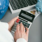 Main calculant le montant d'une facture d'électricien avec une tirelire et un casque de chantier en arrière-plan