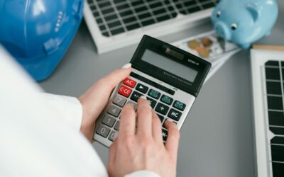 Main calculant le montant d'une facture d'électricien avec une tirelire et un casque de chantier en arrière-plan
