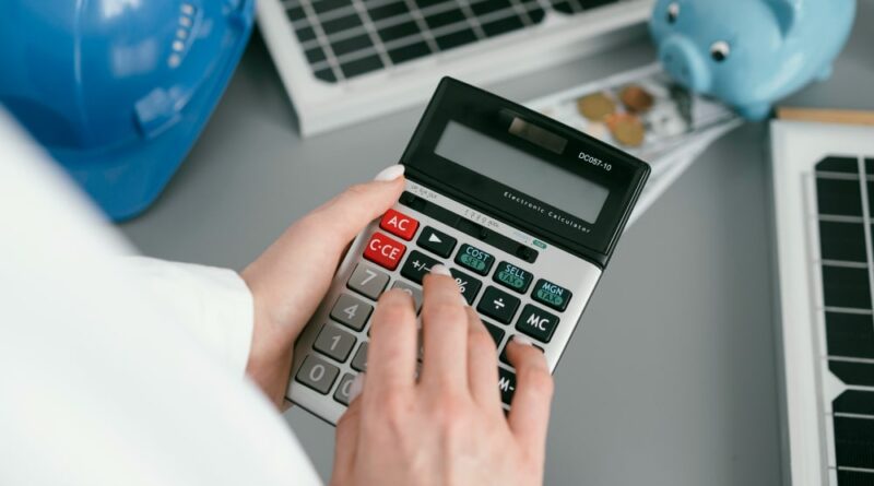 Main calculant le montant d'une facture d'électricien avec une tirelire et un casque de chantier en arrière-plan